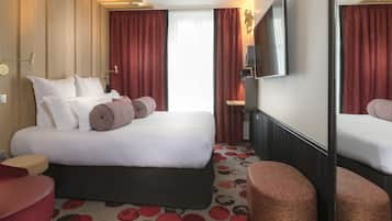 Ett hotellrum med en stor säng, en platt-TV, en spegel och en röd matta med cirkelformade mönster.