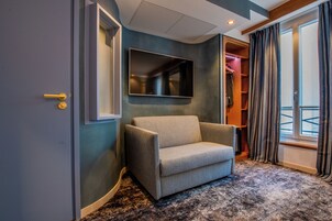 A room with a grey sofa, a mounted TV, a wooden wardrobe, and a window with curtains.