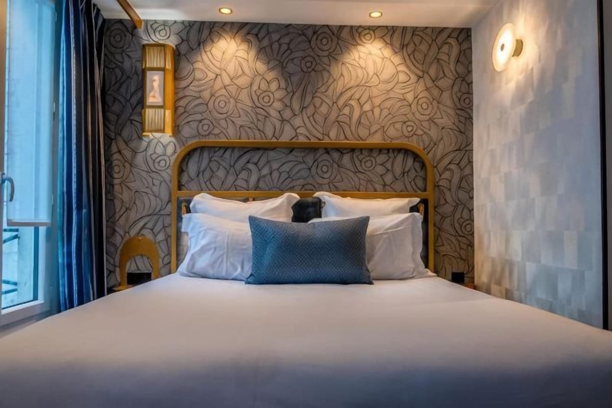 Una cama bien hecha con cabecera, mesita de noche y lámpara de pared.