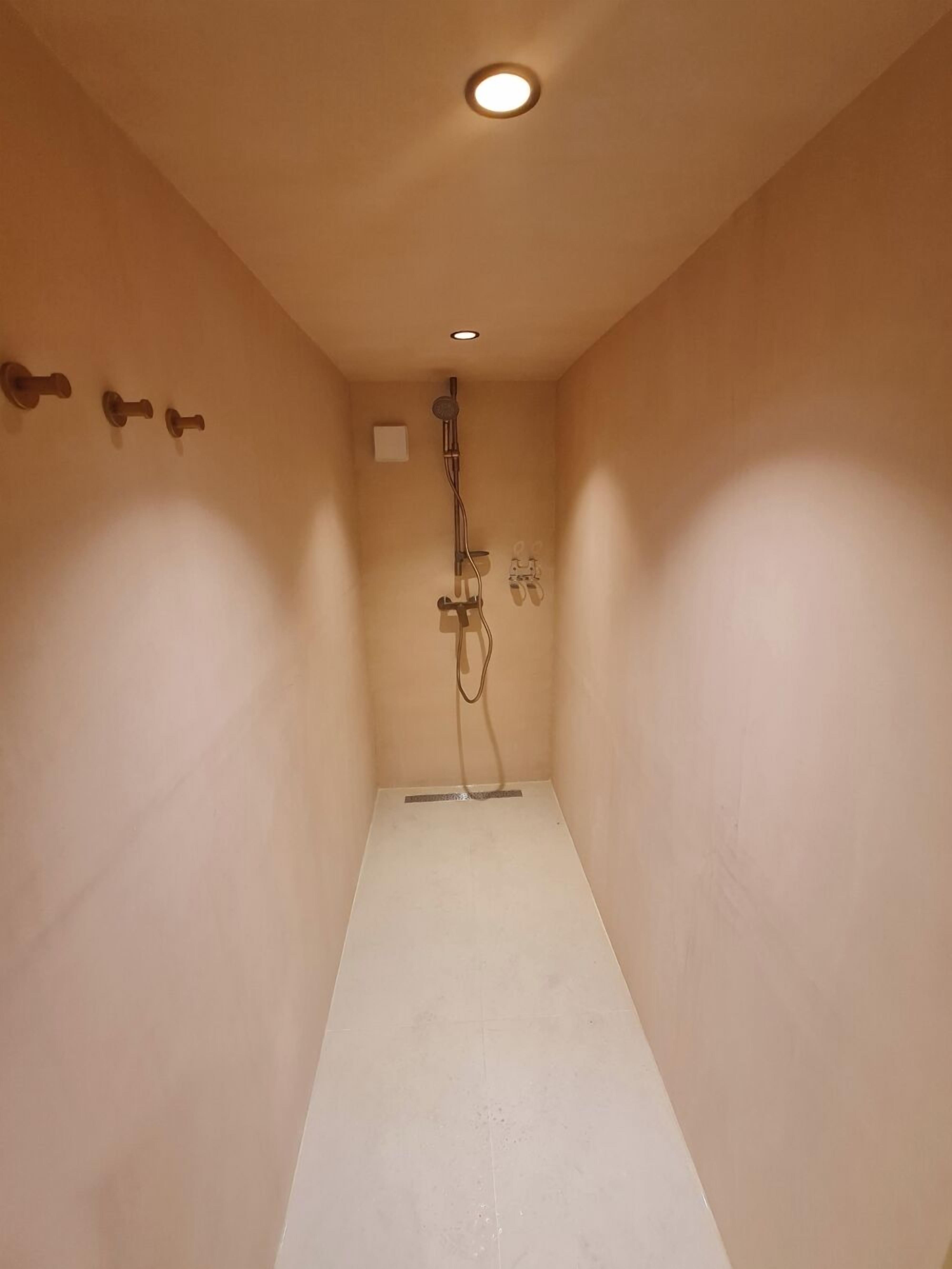 Et aflangt, tomt badeværelse med beige vægge, et hvidt gulv og en loftlampe.