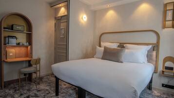 Une chambre d’hôtel avec un grand lit, un bureau avec une chaise, une étagère avec une radio et une porte donnant accès à la salle de bain.