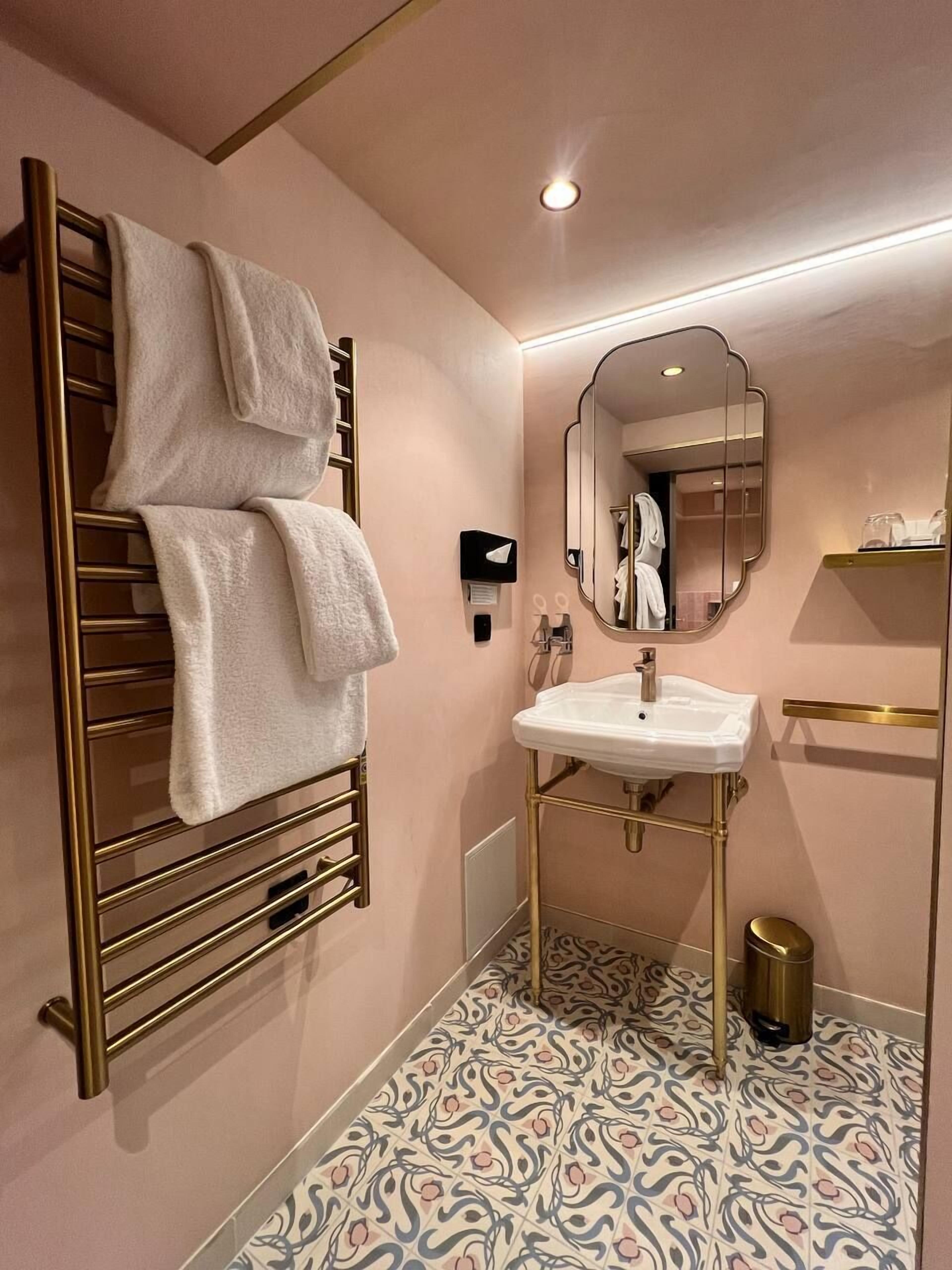 A modern bathroom with a gold towel rack, a white sink, and a patterned floor.