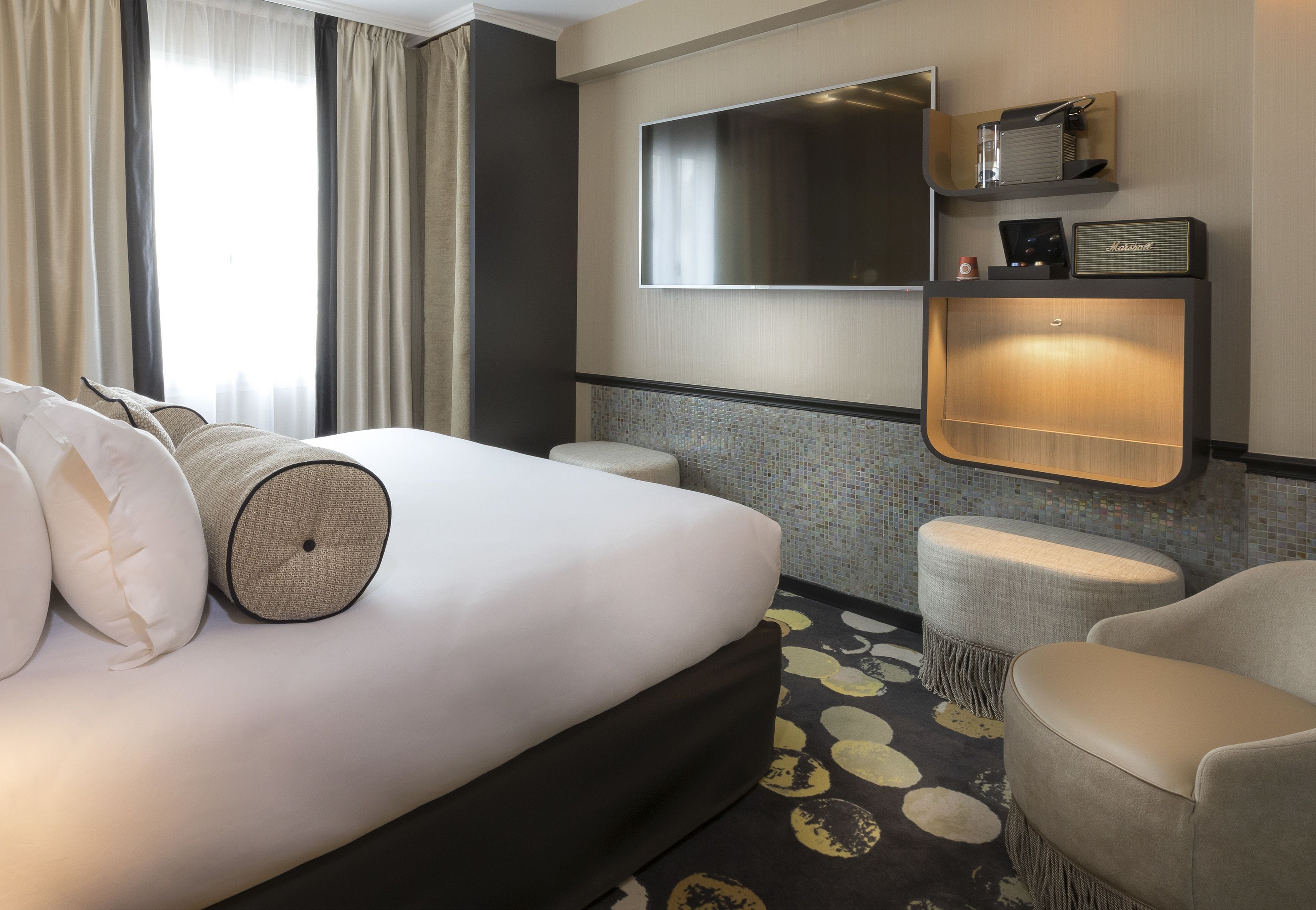 A hotel room with a large bed, a flat-screen TV mounted on the wall, a small shelf with a radio, and a patterned rug.