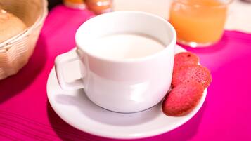 A white cup of coffee on a saucer with a slice of red fruit on the side, set on a pink tablecloth.