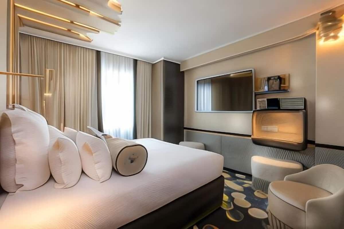 Una habitación de hotel con cama, zona de estar, televisor y estante en la pared.