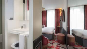Quarto de hotel com um espelho grande, pia branca, cama com cortinas vermelhas e tapete estampado.