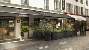 Fachada de hotel con toldo negro, plantas en macetas y un letrero que dice 'CADRAN'.