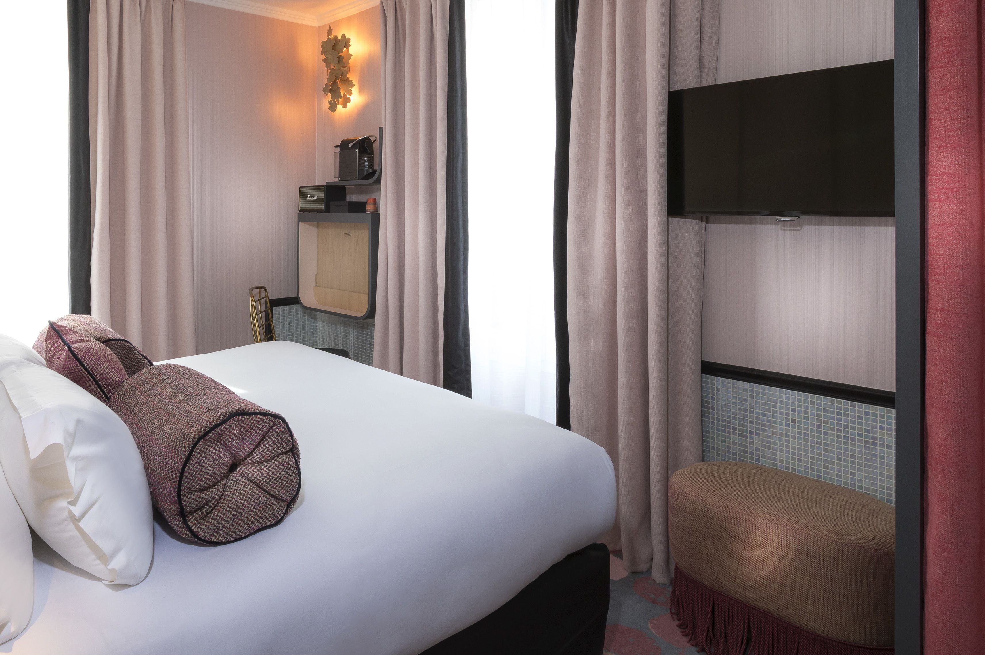 A hotel room with a bed, a bench, a TV, and a small kitchenette.