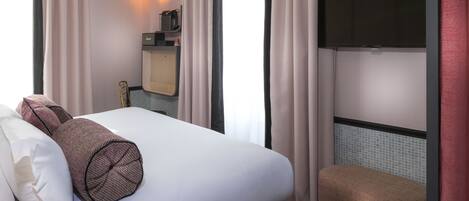 A hotel room with a bed, a bench, a TV, and a small kitchenette.