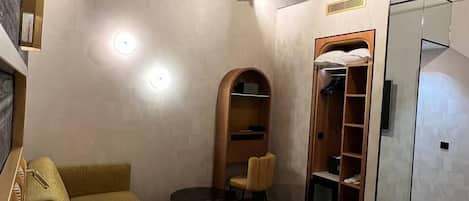 A hotel room with a large bed, a wooden headboard, a small seating area with a chair and table, a wardrobe, and a mirror.