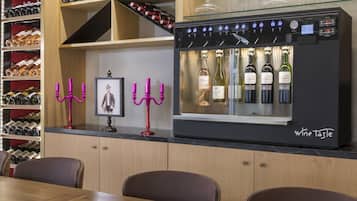 A wine tasting station with a refrigerated display of various wines, a framed artwork, and decorative candelabras.
