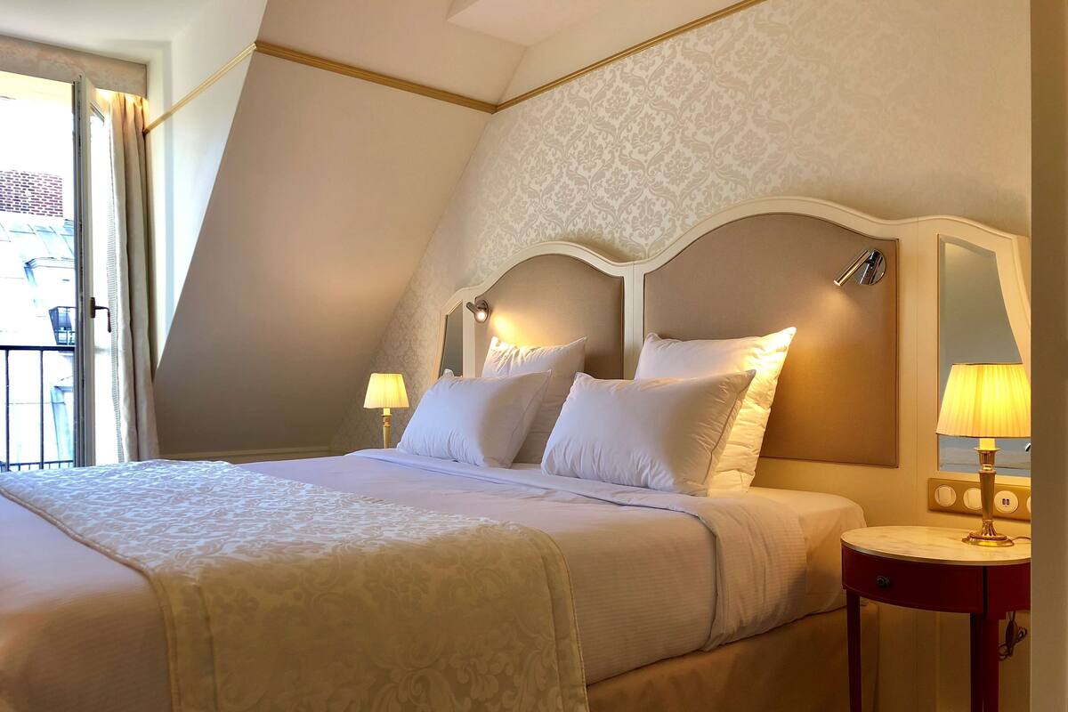 A hotel room with a large bed, two bedside lamps, a nightstand, and a window with curtains.