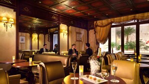 A restaurant with leather booths, tables with candles, and a view of palm trees outside. - Hotel Mayfair (Paris)
