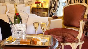 A hotel room with a bed, a red upholstered chair, a tray with a bottle of Moët champagne, two glasses of champagne, and a box of Godiva chocolates. - Hotel Mayfair (Paris)