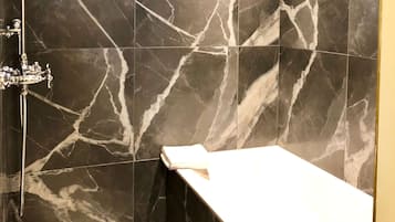 A modern bathroom with dark marble tiles, a shower with a handheld showerhead, and a window above the shower.
