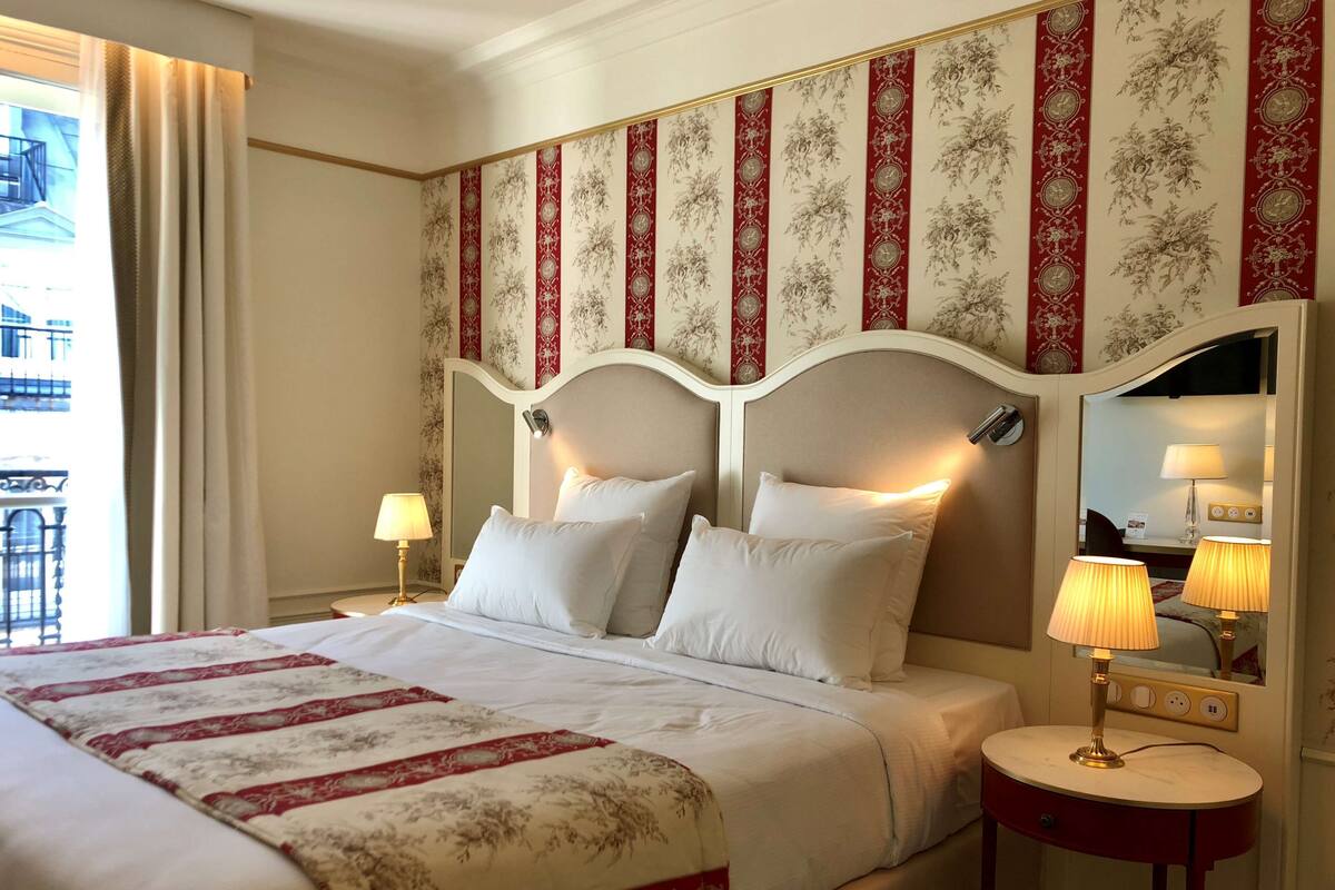 A hotel room with a large bed, two bedside lamps, a round table, and a view of a building outside.