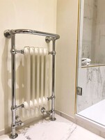 Un bagno con pavimento in marmo bianco, cabina doccia in vetro e porta asciugamani cromata.