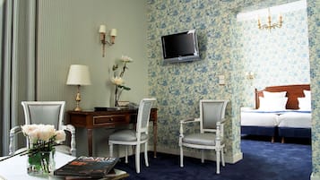 Hotelkamer met een bed, twee stoelen, een bureau, een televisie en een vaas met bloemen.