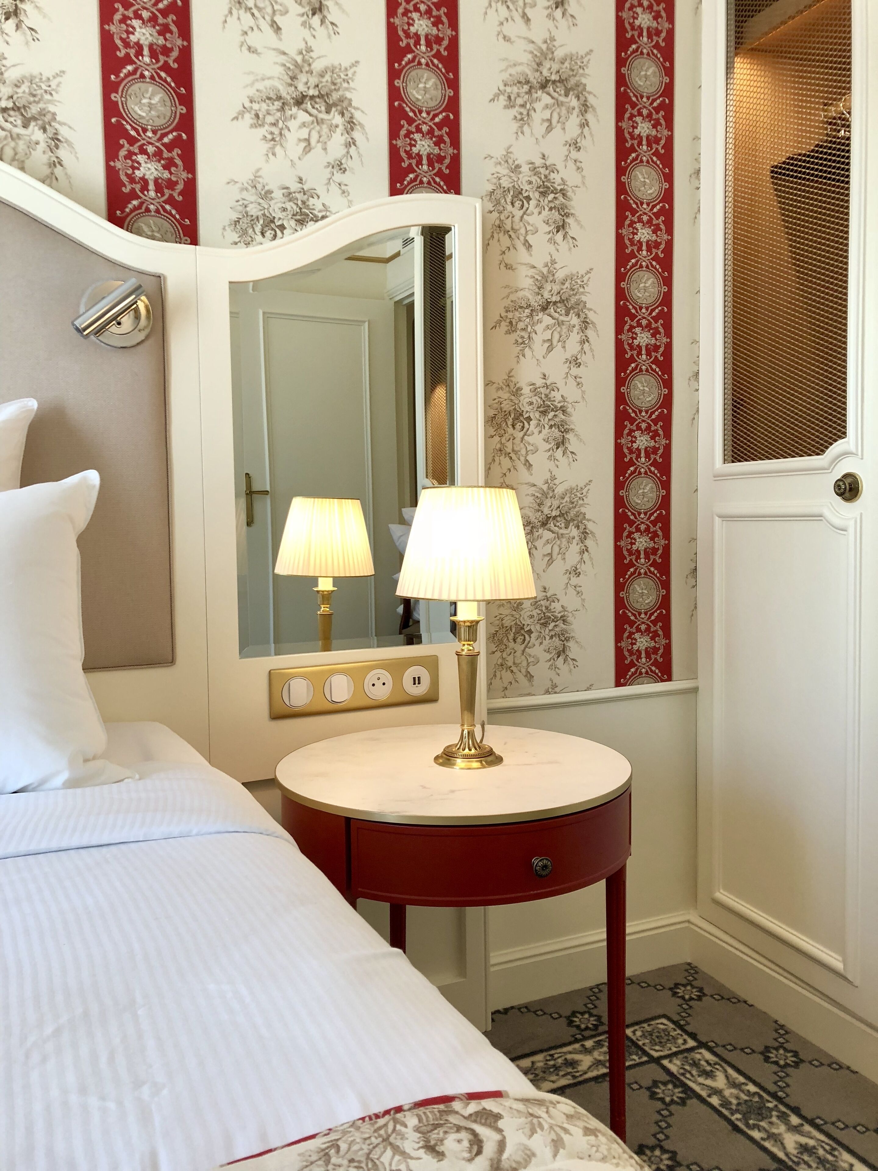 Habitación de hotel con cama, lámpara de noche, espejo y tocador con espejo y marco rojo.