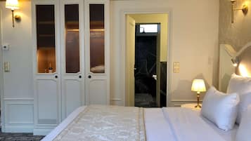 Une chambre d’hôtel avec un grand lit, une armoire aux portes vitrées, une salle de bain visible à travers une porte ouverte et des lampes fixées au mur.