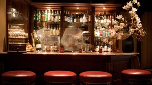 A bar area with a piano, stools, and a variety of liquor bottles. - Hotel Mayfair (Paris)