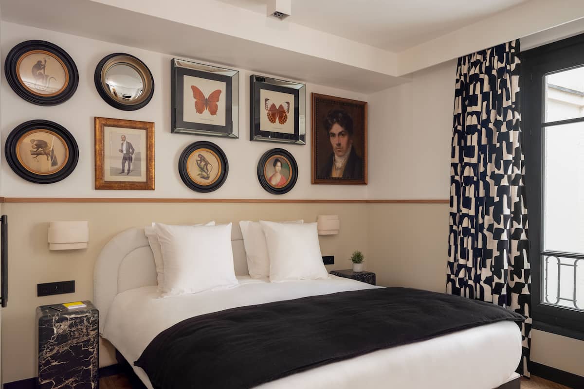Une chambre d’hôtel avec un lit, une table de chevet, un miroir et des tableaux encadrés au mur.