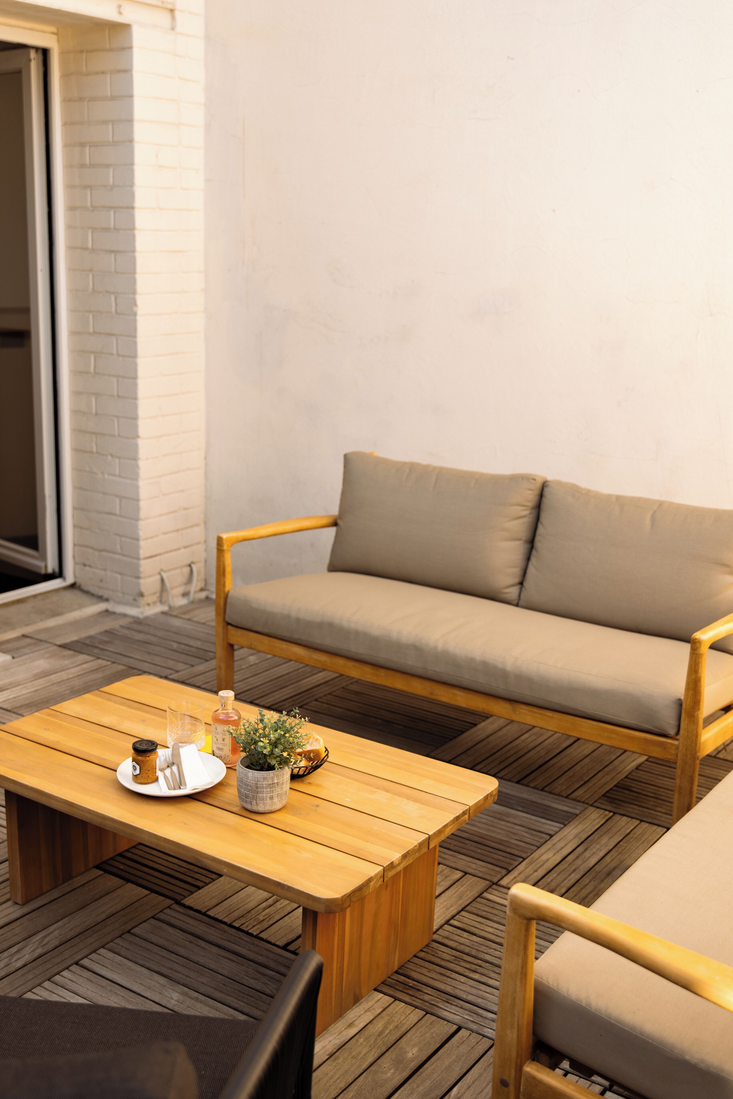 A wooden coffee table with a tray, a beige sofa, and a chair in a cozy outdoor seating area.