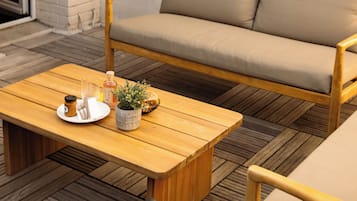 A wooden coffee table with a tray, a beige sofa, and a chair in a cozy outdoor seating area.
