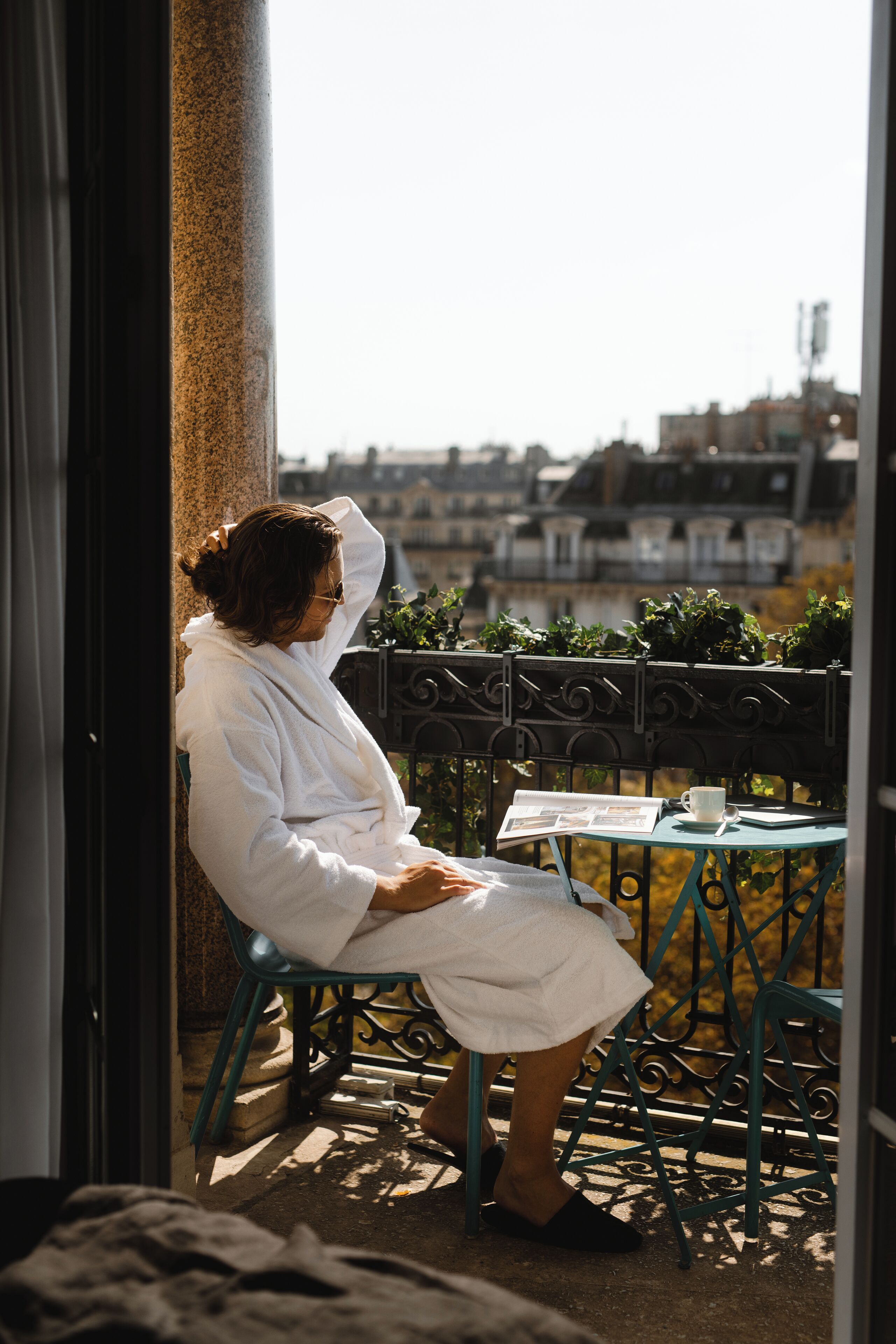 Une personne assise sur une chaise près d’une fenêtre, d’où l’on peut voir des bâtiments.