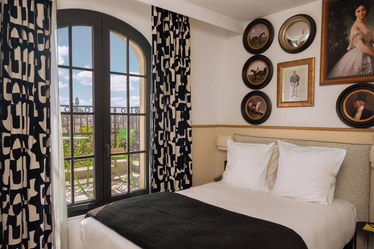 Une chambre d’hôtel avec un grand lit, une vue par la fenêtre et plusieurs tableaux encadrés accrochés au mur.