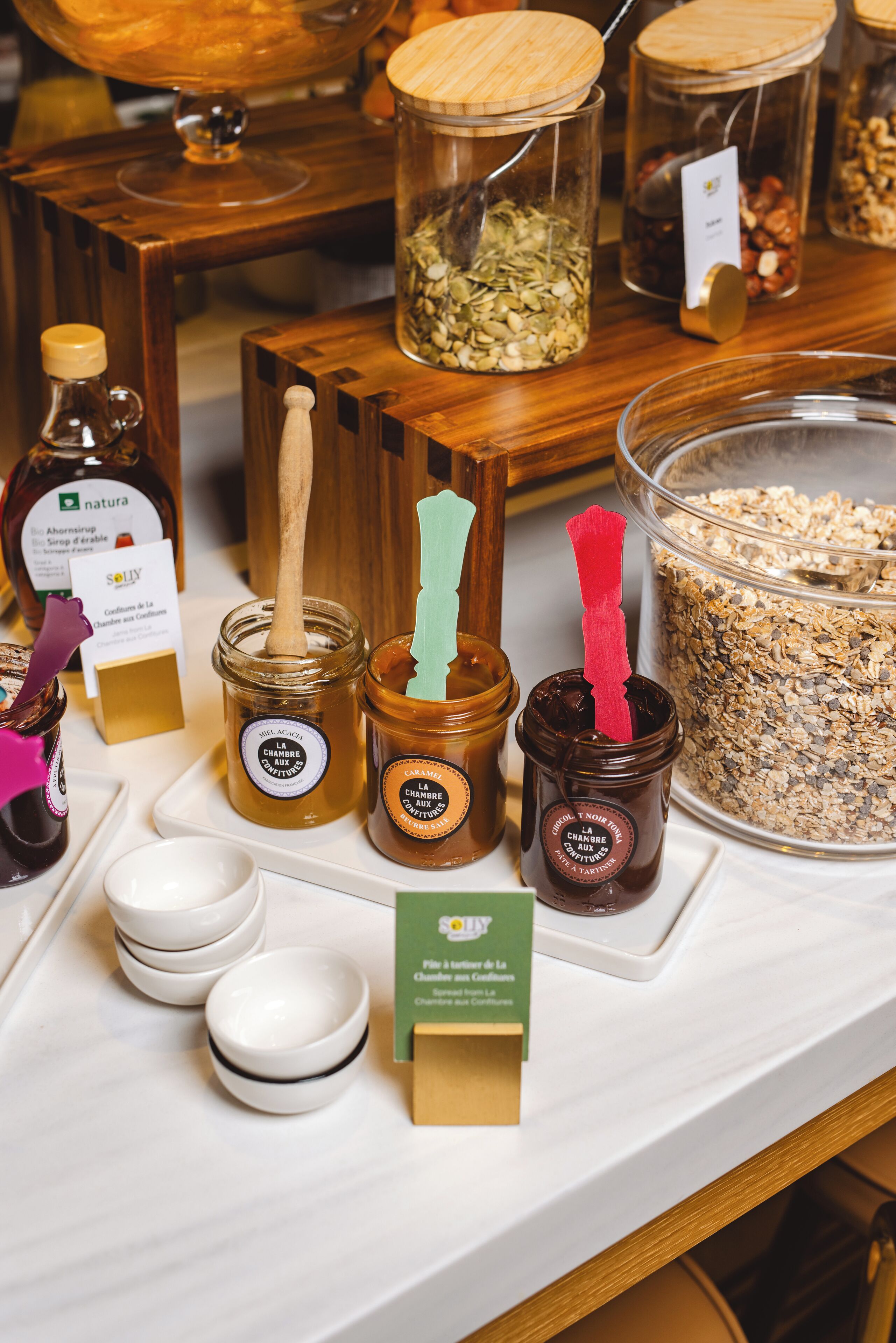 A variety of jars with wooden lids and spoons, some with labels and a card stand.