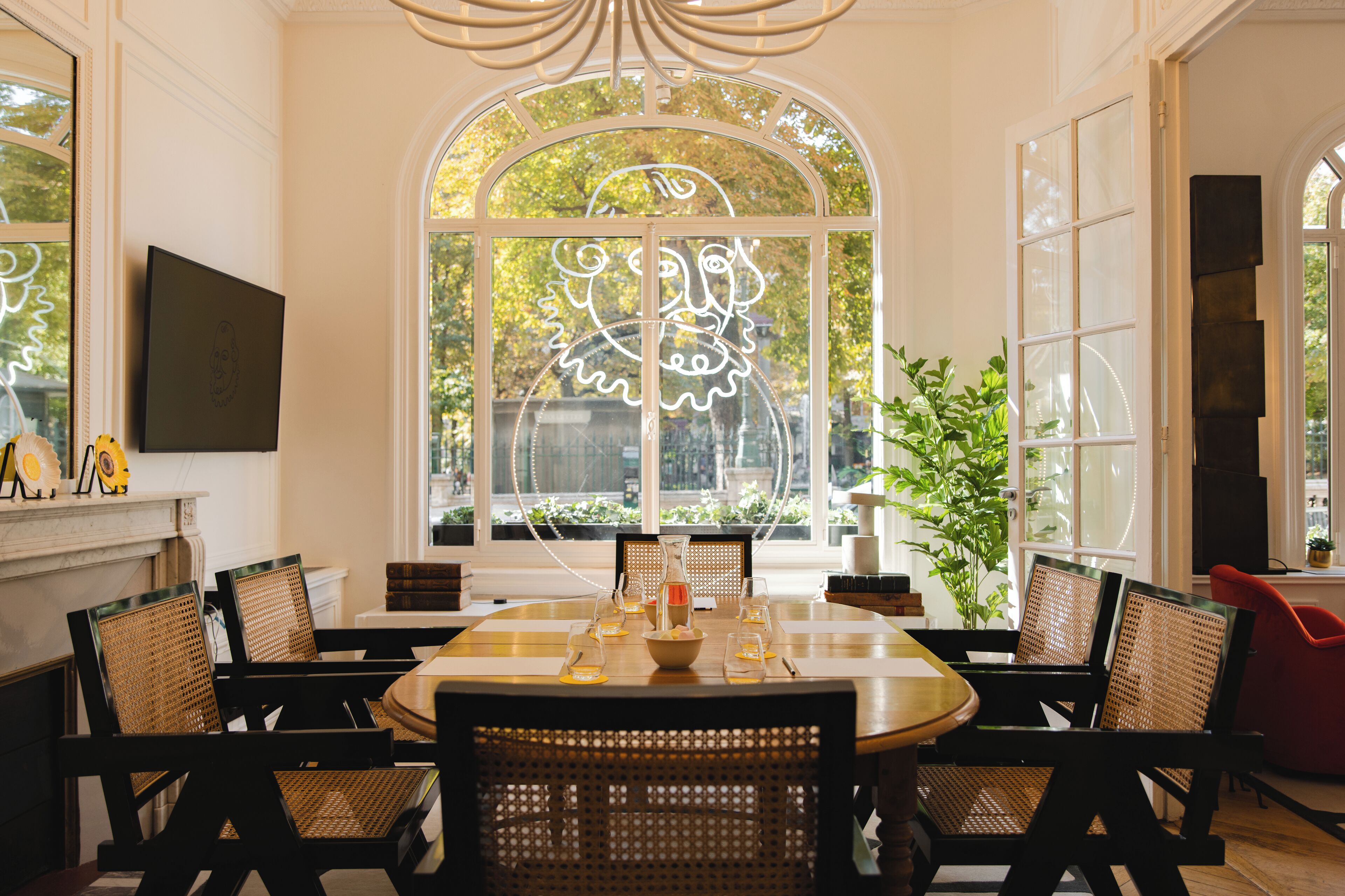 A dining area with a round table, black chairs, and a large arched window with a view of trees.