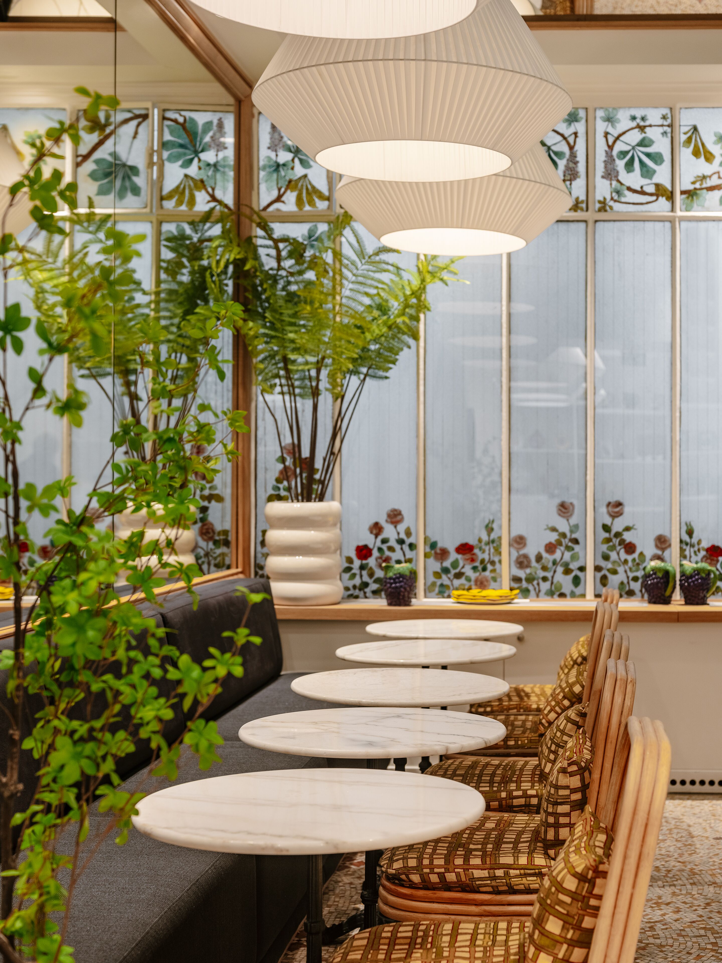 A cozy seating area with a sofa and tables, surrounded by large windows with floral decorations.