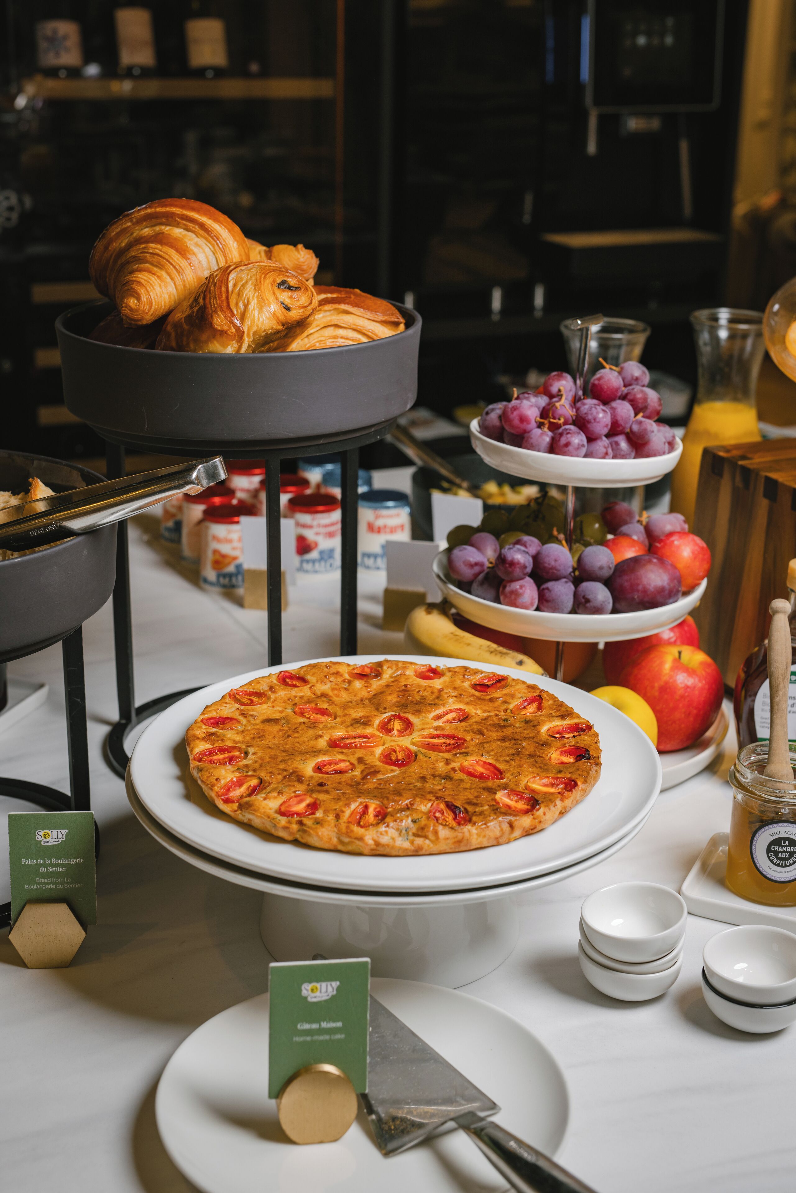 Un buffet de petit-déjeuner avec des croissants, un assortiment de fruits et une pizza.
