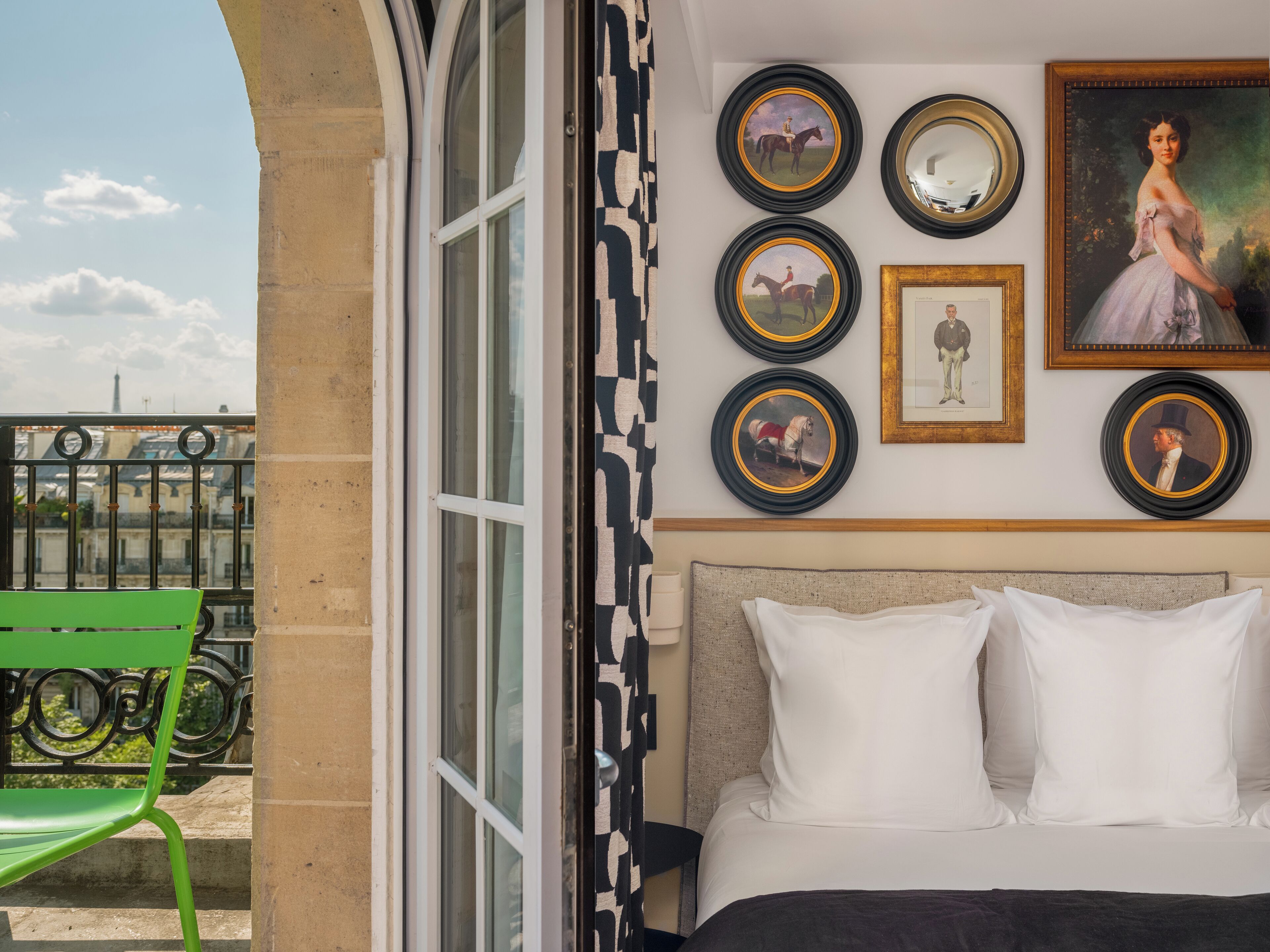 A hotel room with a bed, a green chair, and a wall decorated with framed pictures and mirrors.