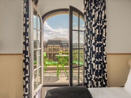 A hotel room with a large arched window, a bed, and a view of a cityscape and greenery.