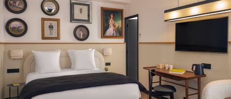 Quarto de hotel com uma cama, mesas de cabeceira, escrivaninha com cadeira, televisão e quadros nas paredes.