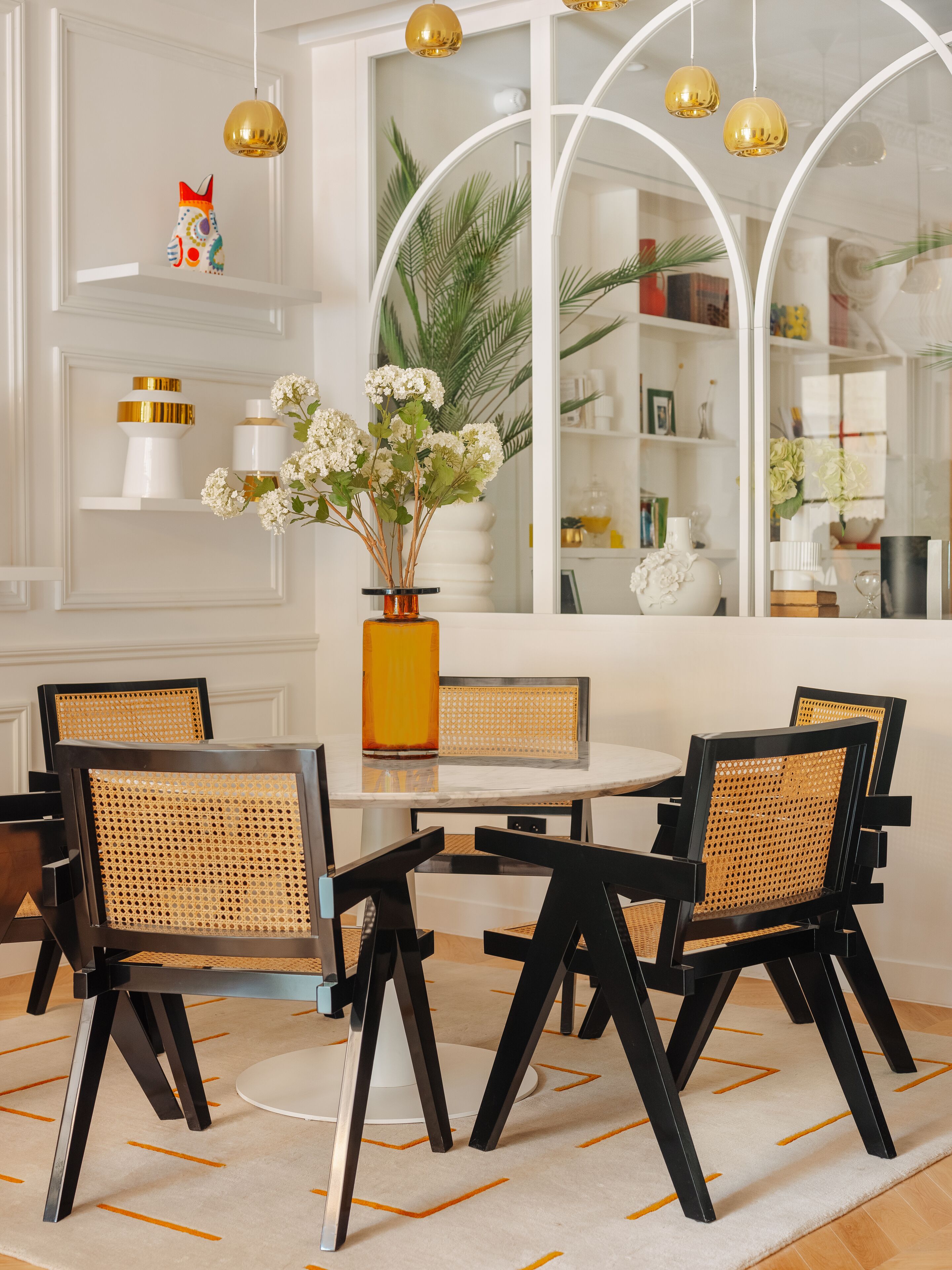A dining area with a round table, black chairs, and a yellow vase with white flowers.