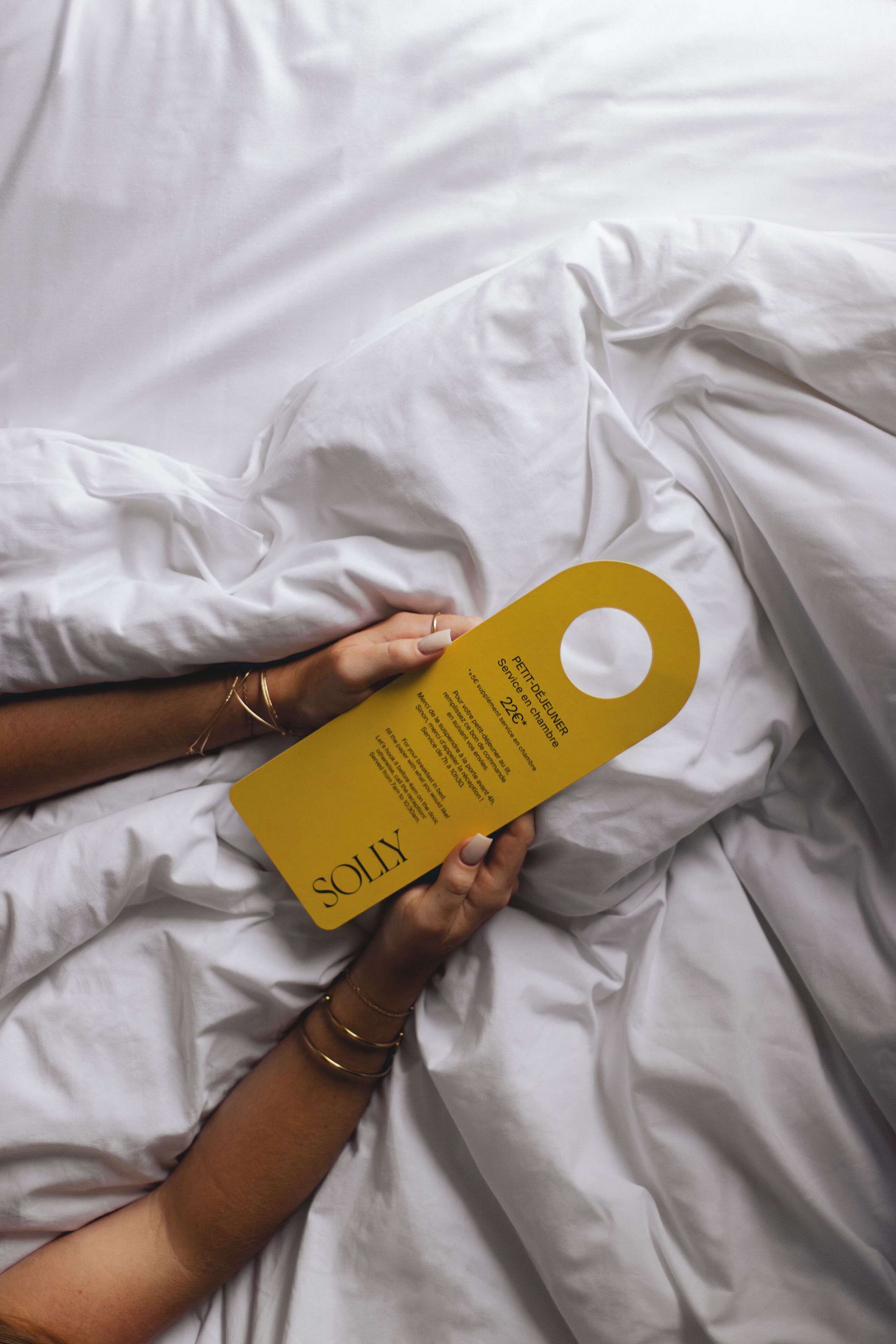 A person lying on a bed holding a yellow tag with text.