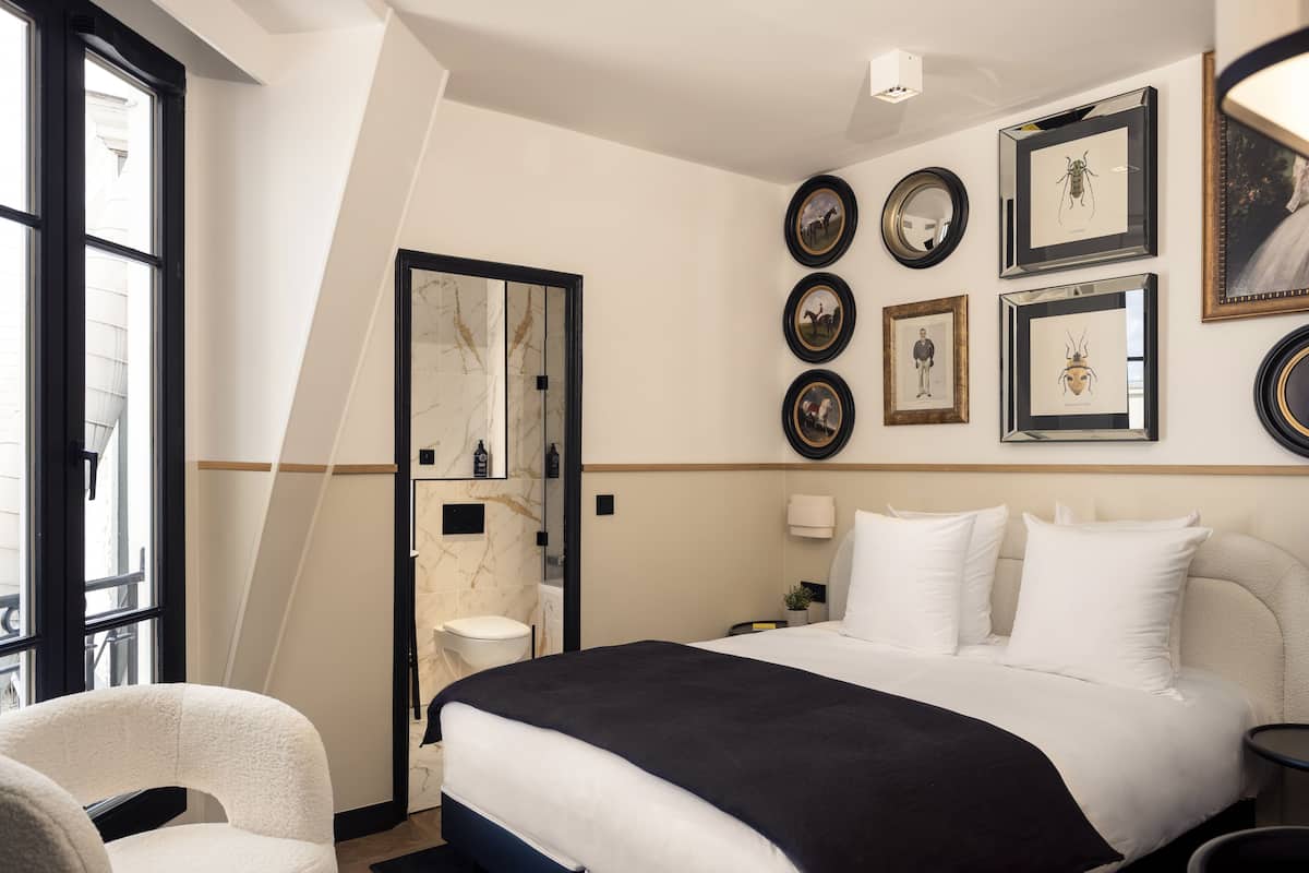 Une chambre moderne dotée d’un grand lit, d’un coin salon avec un fauteuil et d’une salle de bain séparée par une paroi en verre.