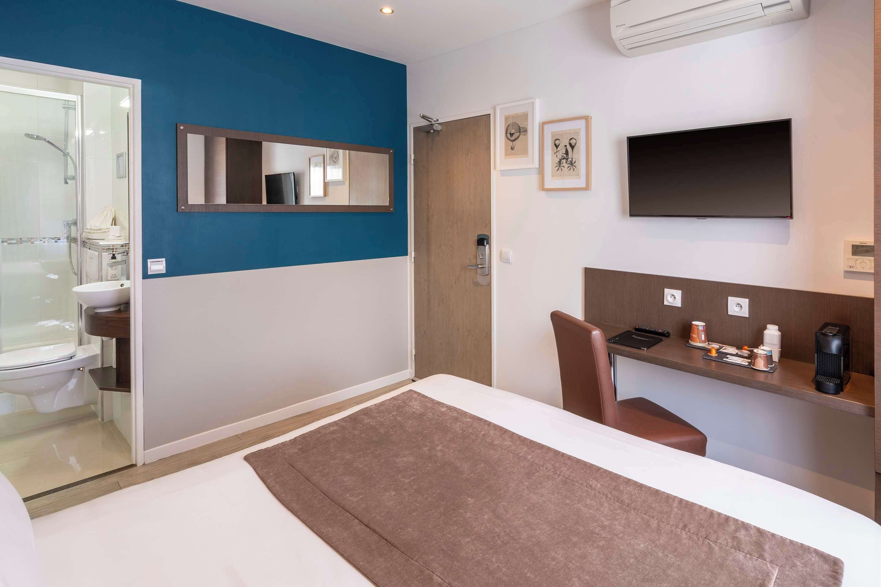 A modern hotel room with a bed, a desk with a chair, a TV, and a bathroom with a shower and toilet.