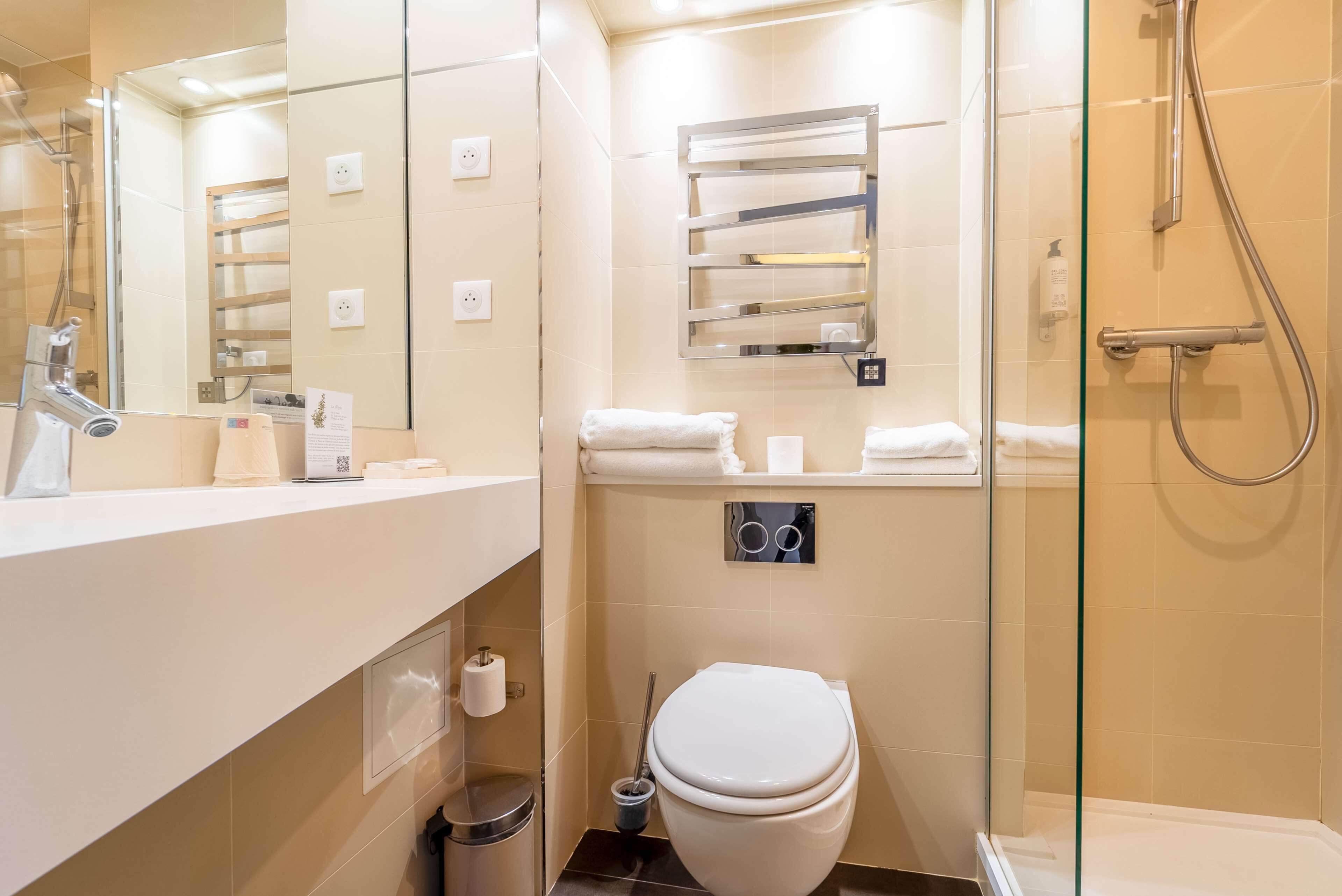 A modern bathroom with a glass shower enclosure, a toilet, a sink with a mirror, and a towel rack.