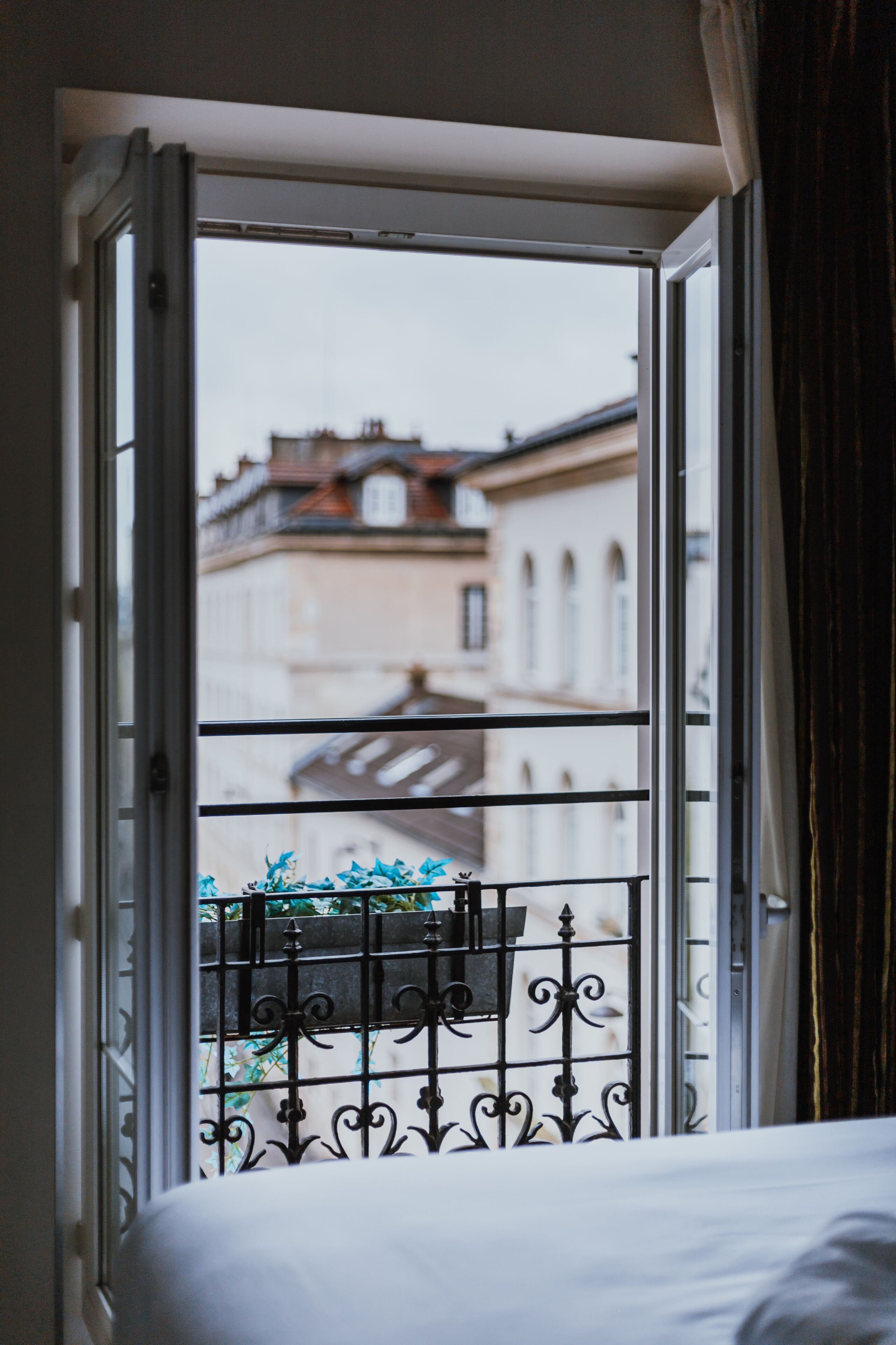 An open window with a view of buildings and a balcony with a metal railing.