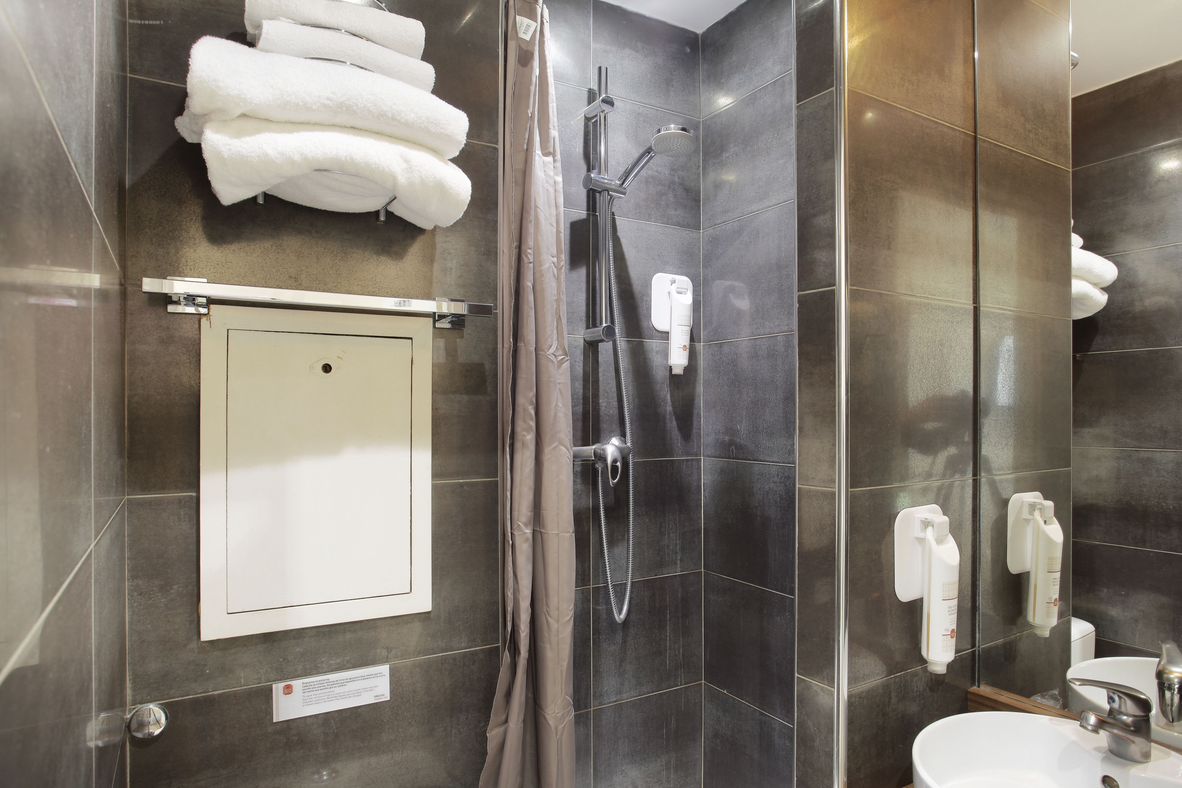 Un baño moderno con cabina de ducha de vidrio, un lavabo blanco y un perchero con toallas dobladas.
