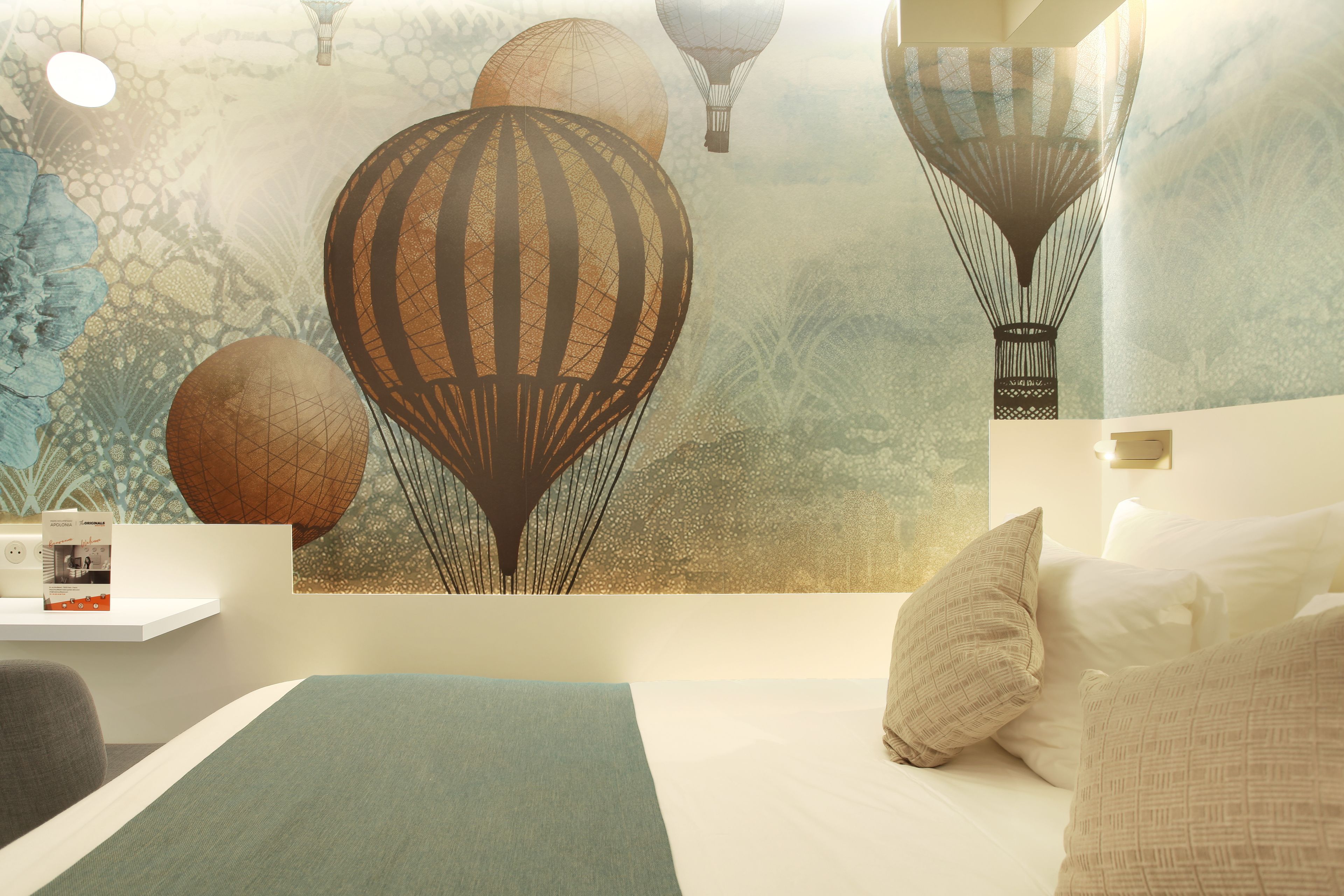 A bedroom with a bed, pillows, a nightstand with a lamp, and a wall mural of hot air balloons.