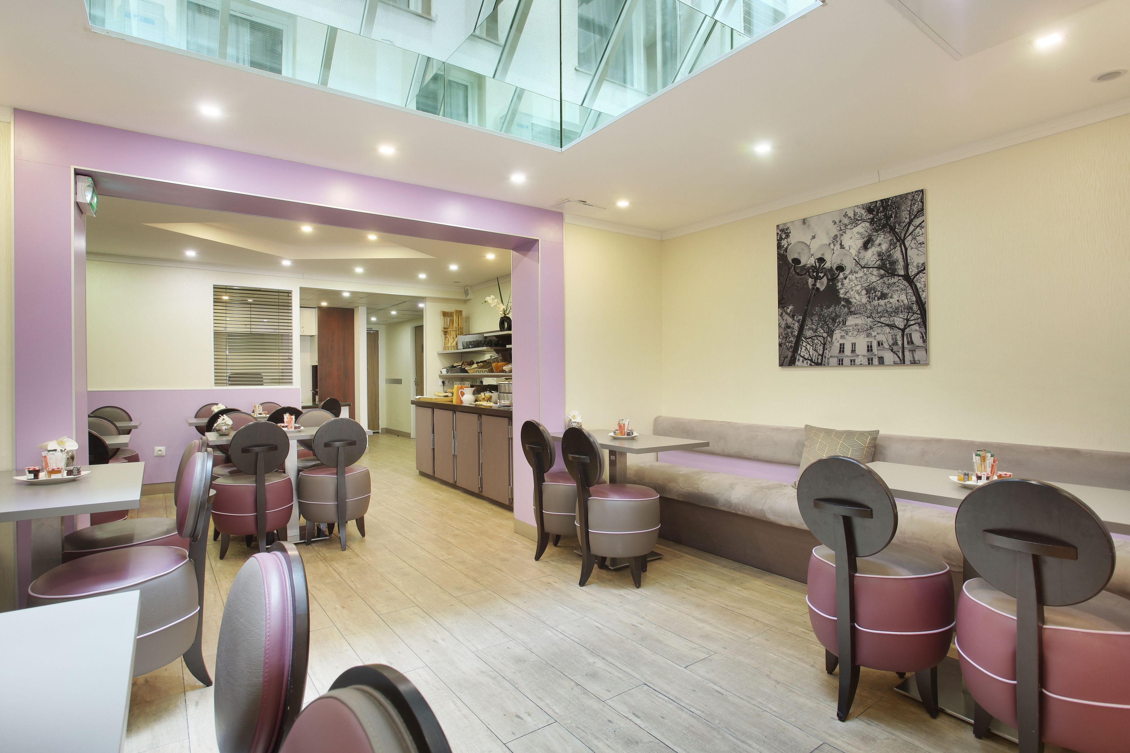 A modern dining area with high ceilings and a skylight, featuring a mix of seating options including tables and a sofa.