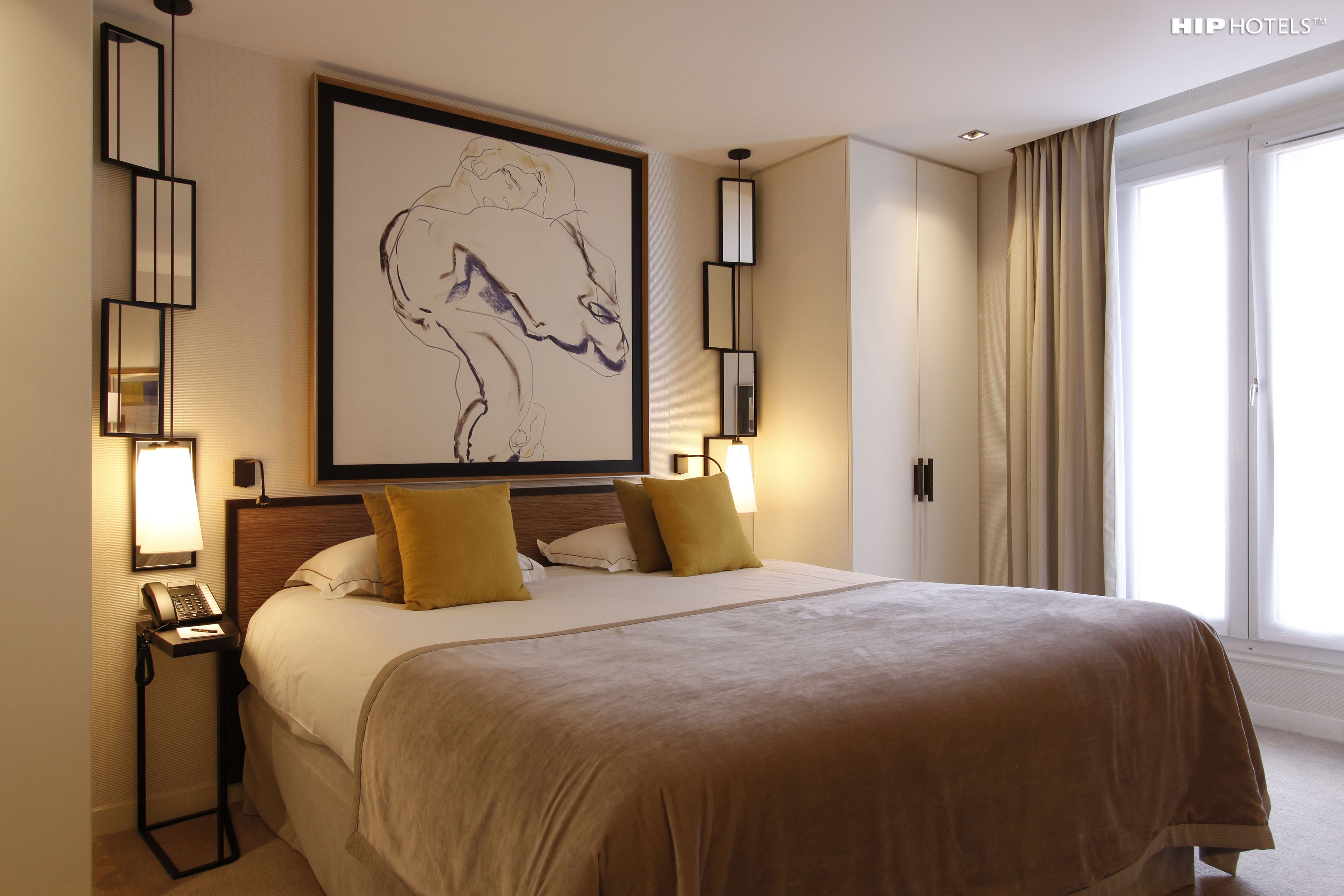 A hotel room with a large bed, two bedside lamps, a framed artwork above the bed, and a window with curtains.