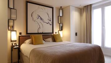 A hotel room with a large bed, two bedside lamps, a framed artwork above the bed, and a window with curtains.