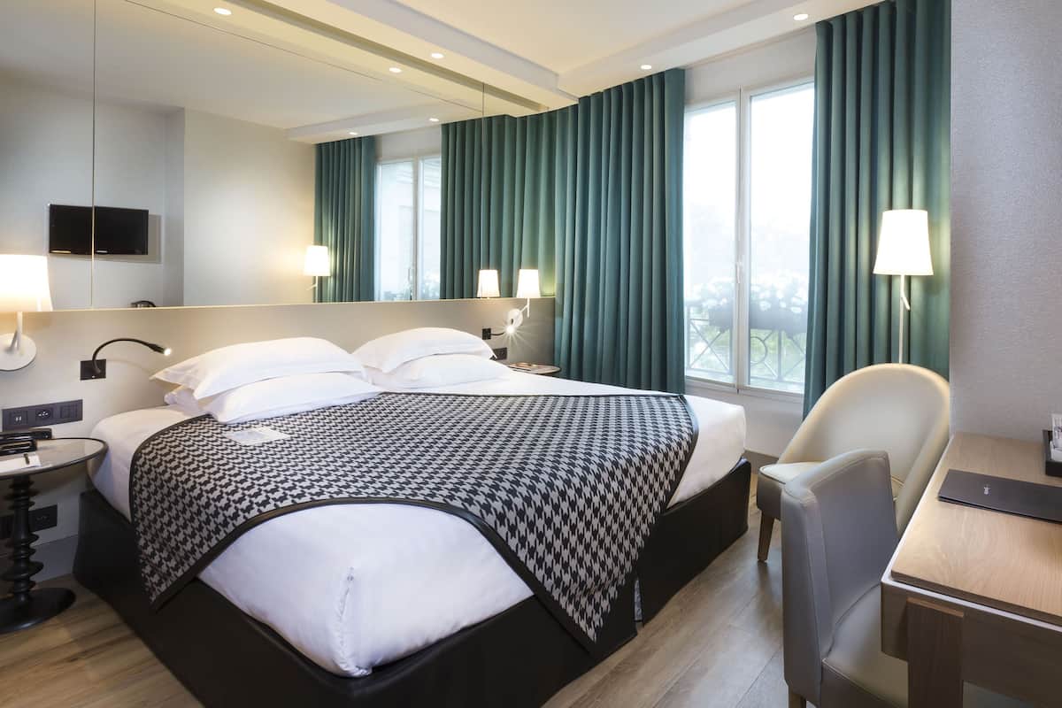 A modern hotel room with a large bed, a desk, a chair, and a TV mounted on the wall.