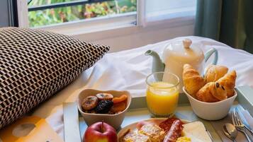 Bandeja de desayuno con cruasanes, fruta y huevos revueltos sobre una cama con vista a la vegetación.